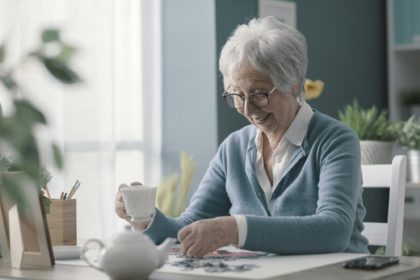 Happy elderly woman solving a puzzle and drinking tea